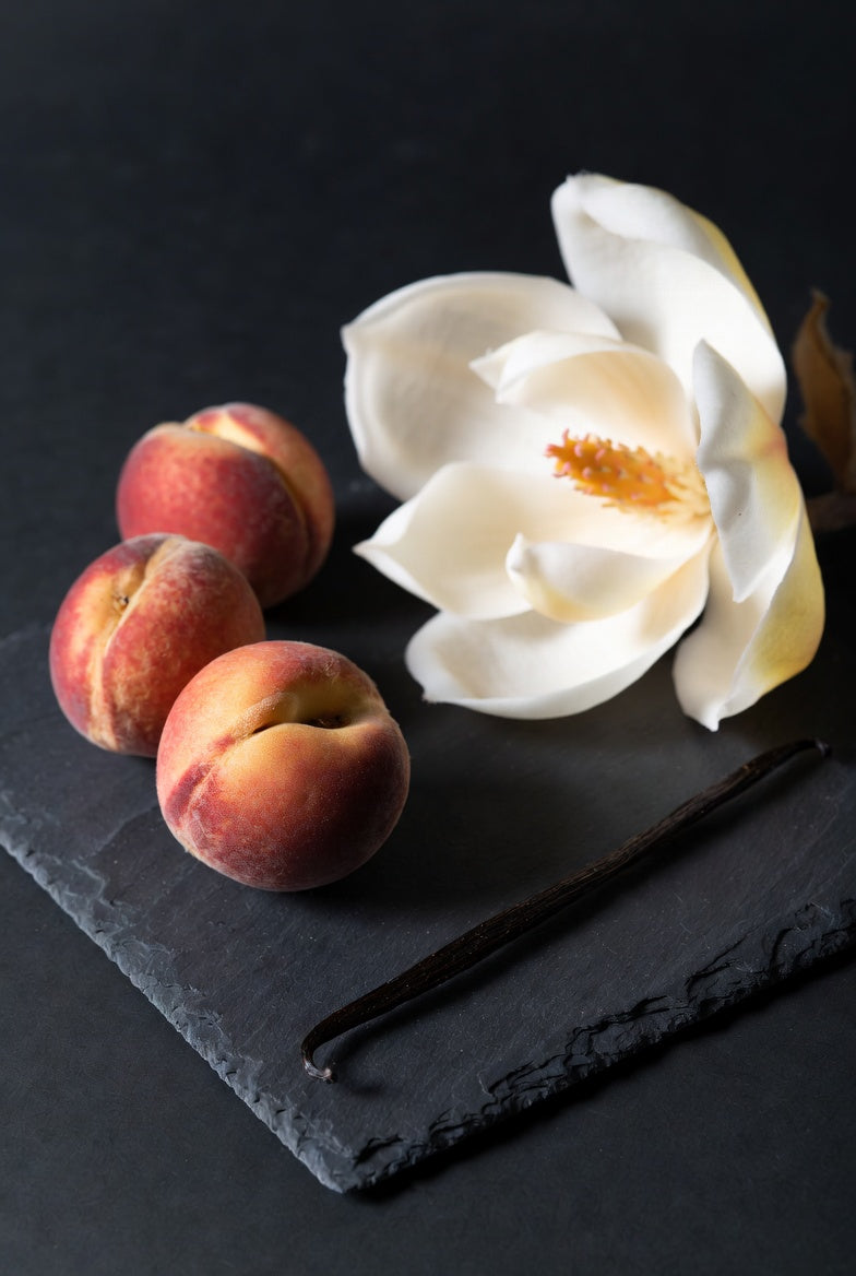 photo of peaches, vanilla pod, magnolia flower on black slate with black background