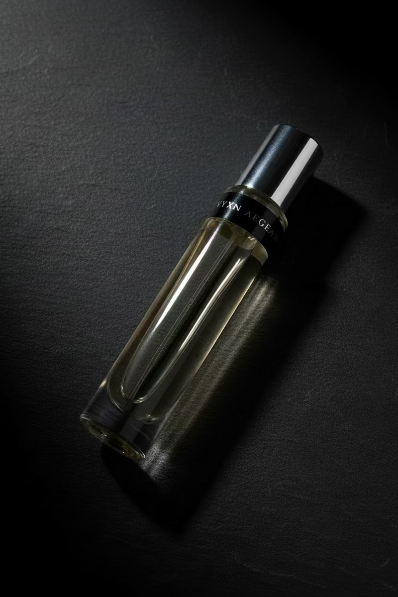 A clear glass perfume roller bottle with a silver cap and a black band, resting diagonally on a dark brown wood grain surface.