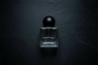 Clear glass perfume bottle with black cap on a dark textured background