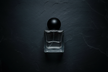 Clear glass perfume bottle with black cap on a dark textured background