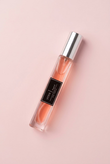 A clear rectangular perfume bottle filled with peach-pink liquid, featuring a black label with white text and a reflective silver cap, set against a draped light pink satin fabric background.