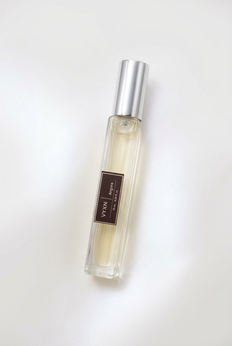 A clear rectangular perfume bottle filled with pale yellow liquid, featuring a black label with white text and a shiny silver cap, set against a draped light pink satin fabric background.