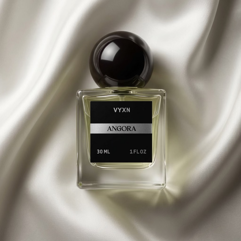 A 30ml bottle of VYXN Angora perfume, featuring a clear glass square bottle with pale yellow liquid, a black label with silver lettering, and a dark brown spherical cap, set against a shiny light pink satin background.