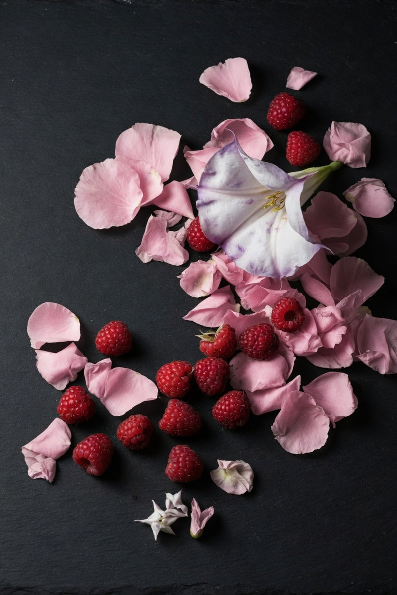 pink rose petals, datura flower and raspberries on black slate background