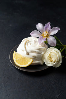 White meringue dessert with a lemon wedge and flowers on a dark background